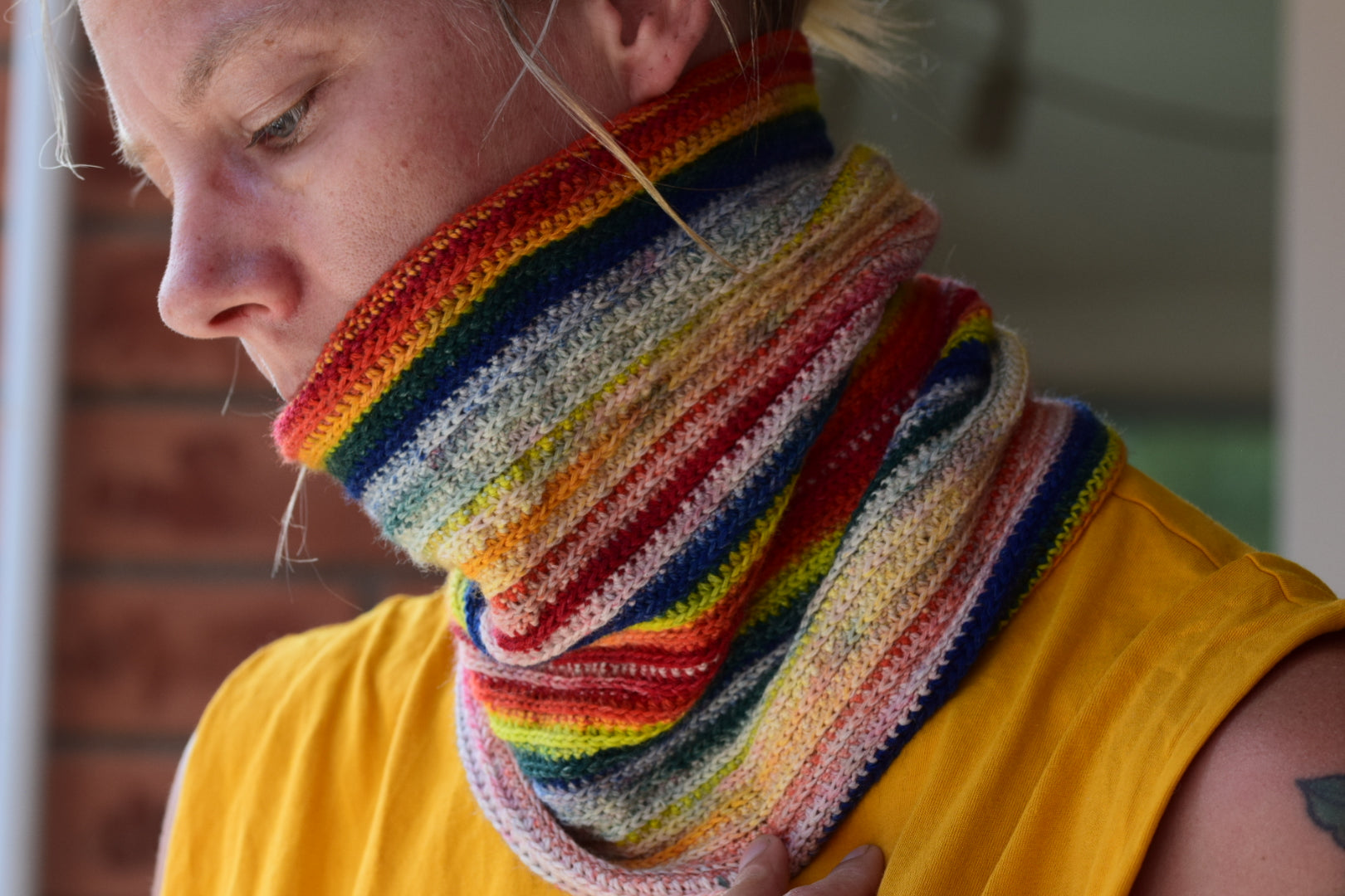 Person som bär en färgstark, handstickad halskrage i regnbågens färger – exempel på stickat nybörjarprojekt med garn från Garnverkstan.