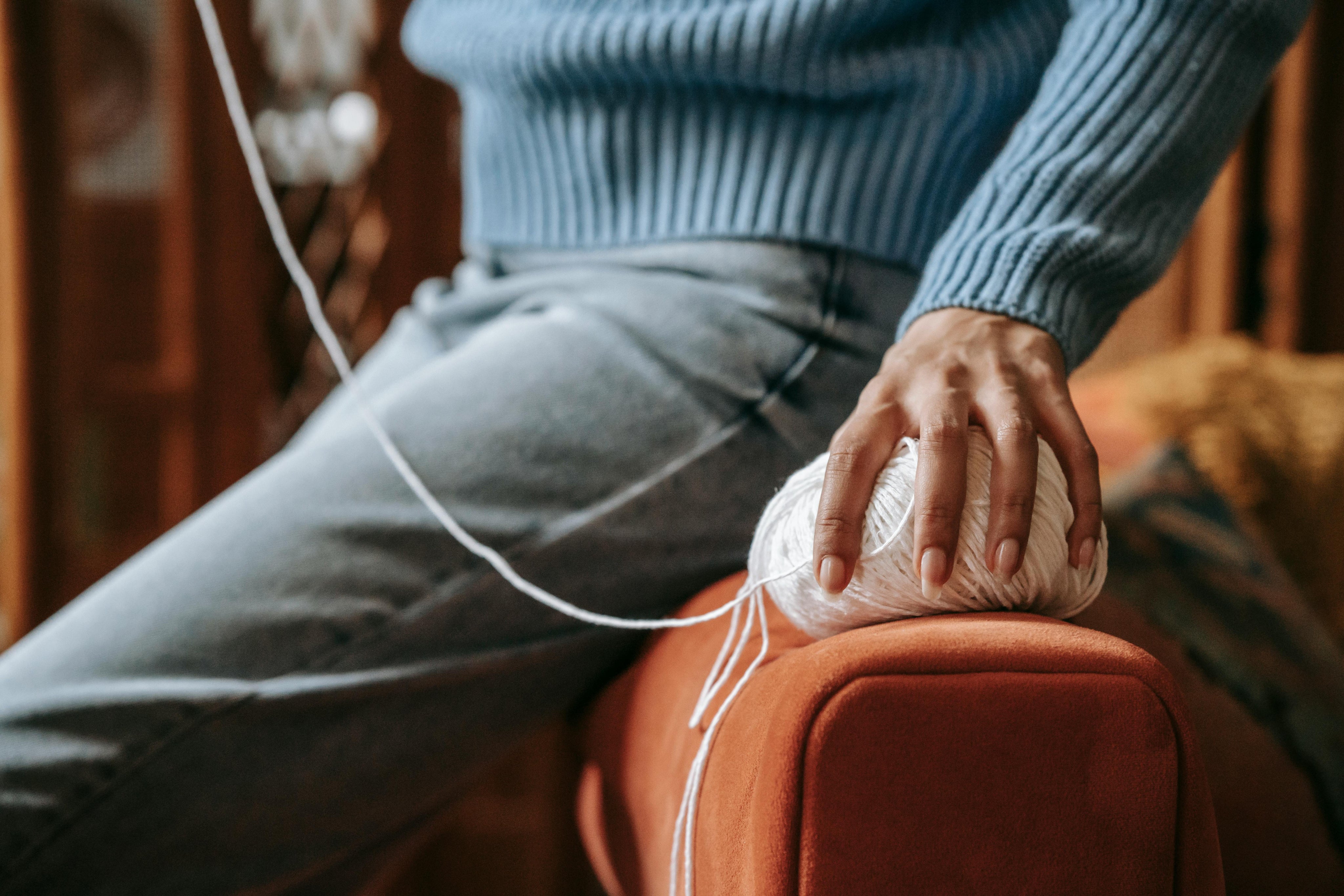 Person som sitter på soffkant med garn i handen