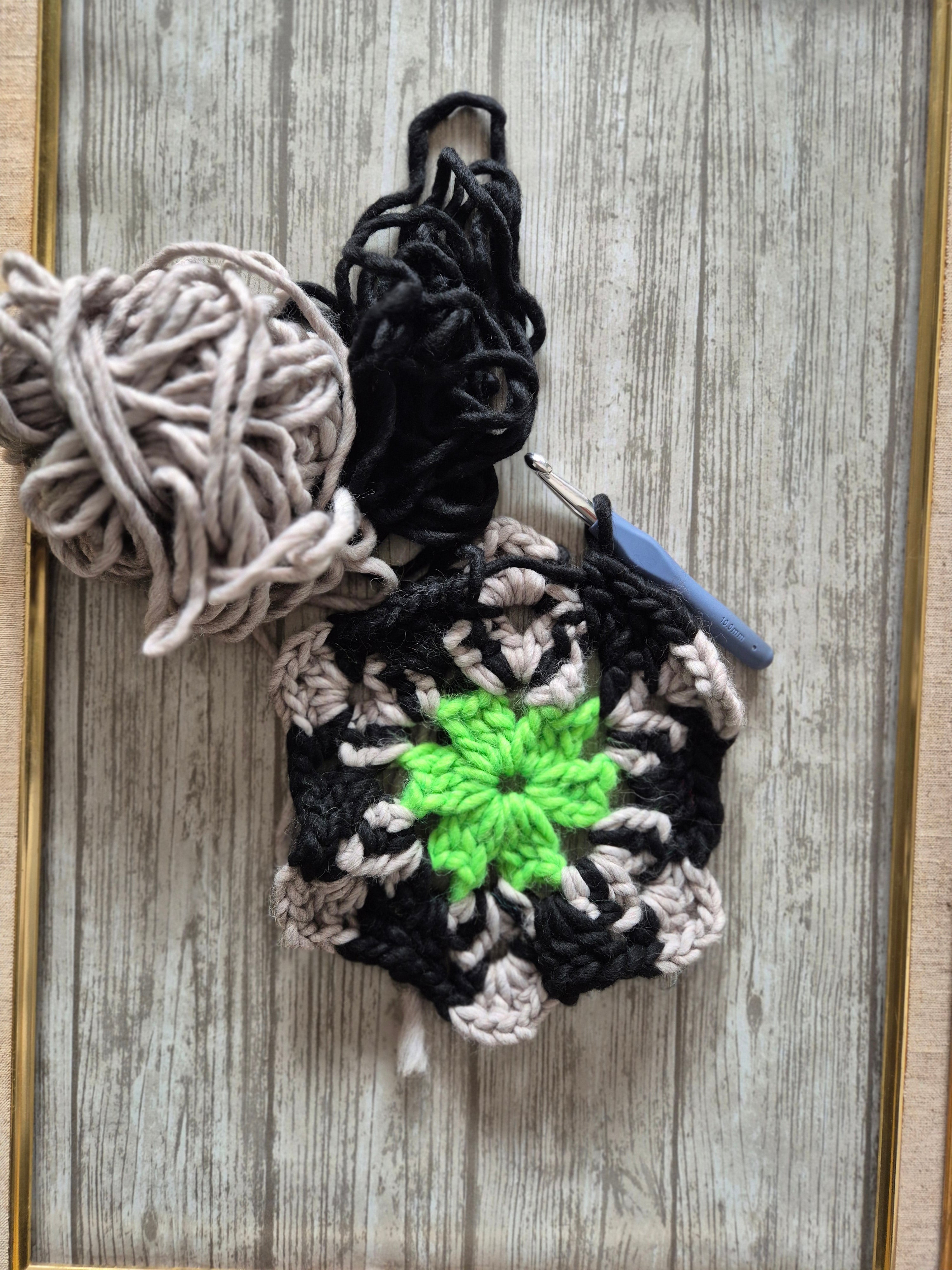 Påbörjad virkad ruta i grönt, svart och beige Katia-garn med virknål på träunderlag.