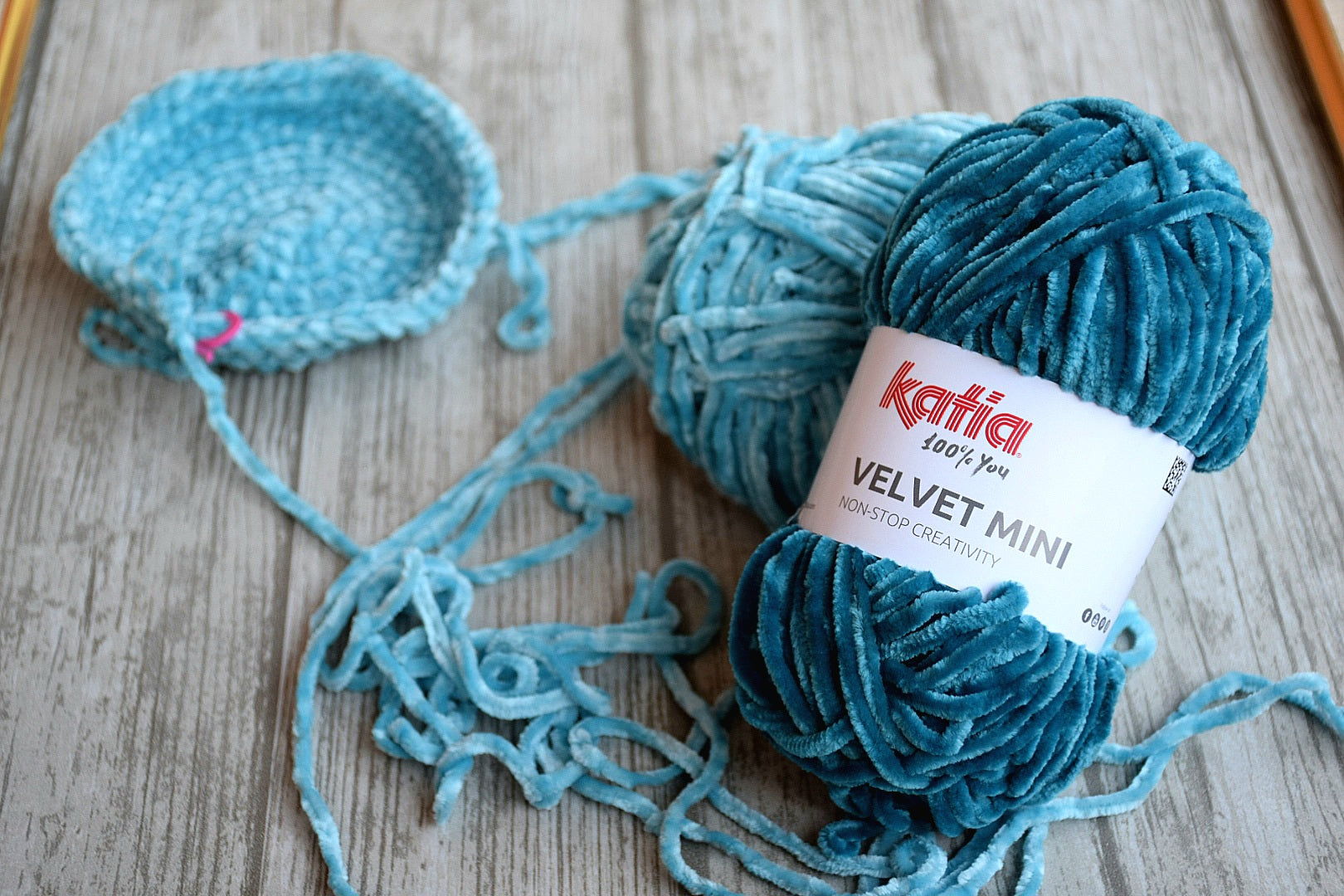 Katia Velvet Mini garn i mellanblå och jeans nyans tillsammans med påbörjat virkat arbete på träbord.